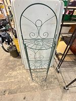 Front view of green metal plant stand with three round shelves and scrollwork