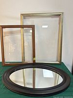 All three frames standing: gold rectangular, brown rectangular with cracked glass, dark brown oval mirror
