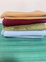 Stack of five folded blankets in tan, burgundy, green, light blue, gray