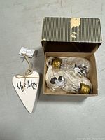 Heart ornament with tag beside open box containing two decorative glass bulbs