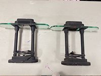 Two identical black metal table lamps lying on their sides showing bases, columns, glass shades and power cords