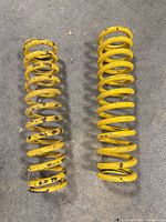 Two yellow coil springs laid side-by-side showing overall condition