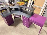 Overall view of purple and black L-shaped desk showing two drawer pedestals, return section and raised monitor shelves