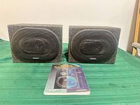 Front view of both Sony speakers inside carpeted enclosures with manual in foreground