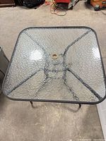 Top view of square glass patio table showing metal frame and umbrella hole