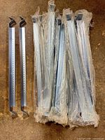 Bundled stack of approximately twenty steel galvanized wall mount brackets in plastic with two loose brackets showing perforations