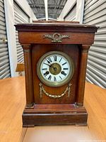 Front view of wooden mantel clock showing dial, bezel, columns and brass ornaments