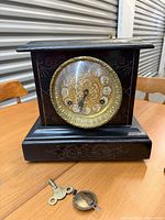 Front view showing clock case, brass dial, bezel, key and pendulum