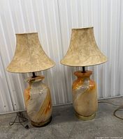 Both porcelain lamps with tan shades displayed side by side