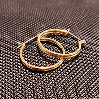 two gold-tone sterling silver hoop earrings overlapping on textured background