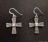 Front view of both sterling silver cross earrings on textured background