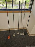 Six clubs leaning against wall displaying heads and shafts