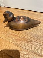 Left side profile of wooden duck decoy on wood floor