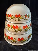 Stacked view of three strawberry pattern enamel bowls showing exterior decoration