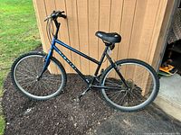 Full side view of blue Nishiki Bravo mountain bike leaning against shed.
