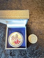Colorized 1999 American Silver Eagle in blue presentation box beside bicentennial medallion