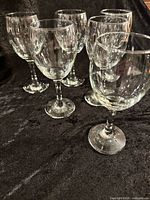 Six clear glass wine goblets grouped on black surface