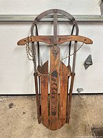 Full view of sled showing wood slats, metal runners, steering bar, rope