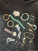 Overview of entire lot on black background showing watch, brooches, bracelets and earrings