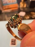 Side view of ring showing marquise green stone in halo setting and gold band
