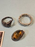 Front view of three sterling pieces: horse head ring, Celtic knot ring, tiger’s eye clip-on earring