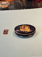 Closed oval cobalt blue Limoges trinket box beside postage stamp for scale