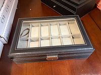 Closed watch box showing exterior, glass lid, stitching and clasp