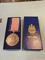 Medal in presentation box with lid beside showing crest and dates