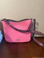 Front view of pink Coach pebbled leather crossbody bag with burgundy strap and gold logo