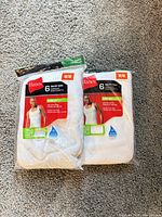 Two sealed 6-packs of Hanes tagless tanks on carpet
