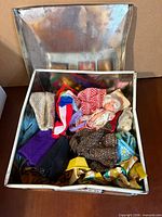Open metal box showing mixed doll clothes and small doll inside