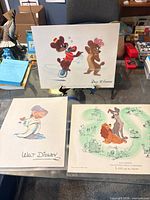 Three Disney lithographs displayed together on table