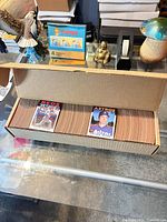 Open cardboard storage box showing two rows of baseball cards with Pete Rose and Nolan Ryan cards on top