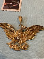 Front view of gold eagle pendant next to postage stamp for scale