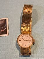 Front view showing round dial, bracelet and stamp for scale