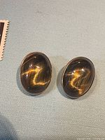 Front view of both oval tiger’s eye clip-on earrings showing chatoyancy and gold bezel
