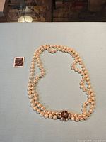 Full view of double strand pearl necklace alongside postage stamp for scale