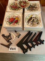 Overview of five porcelain collector plates in Styrofoam trays with wooden and plastic stands