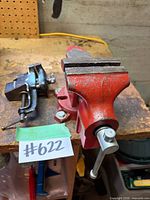 Infact red swivel-base bench vise and smaller clamp-on vise on workbench