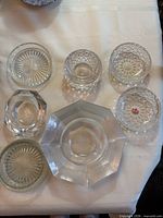 Six clear glass dishes and ashtrays laid out on table