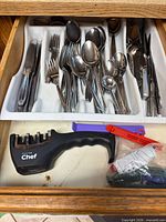 Flatware in drawer organizer; knife sharpener and bag clips visible