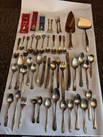 Full assortment of flatware laid out on paper including spoons, forks, servers, packaged souvenir spoons