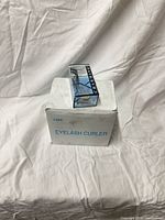 Closed white carton marked 12PC Eyelash Curler with one packaged curler displayed on top