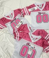 Four pink and white NFL baby jerseys laid out showing teams and tags