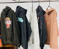 All five hoodies hung on rack showing colors and graphics