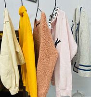 Front view of five assorted women's sweaters hanging