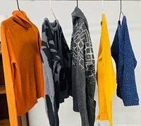 Five sweaters hanging side-by-side showing colors and patterns