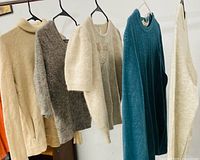 Five women’s sweaters hung on hangers showing colors and styles