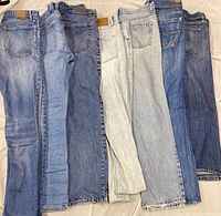 Front view of seven pairs of men’s denim jeans laid side by side showing washes and waistband patches