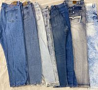 Seven pairs of assorted men’s jeans laid side-by-side showing front and wash differences